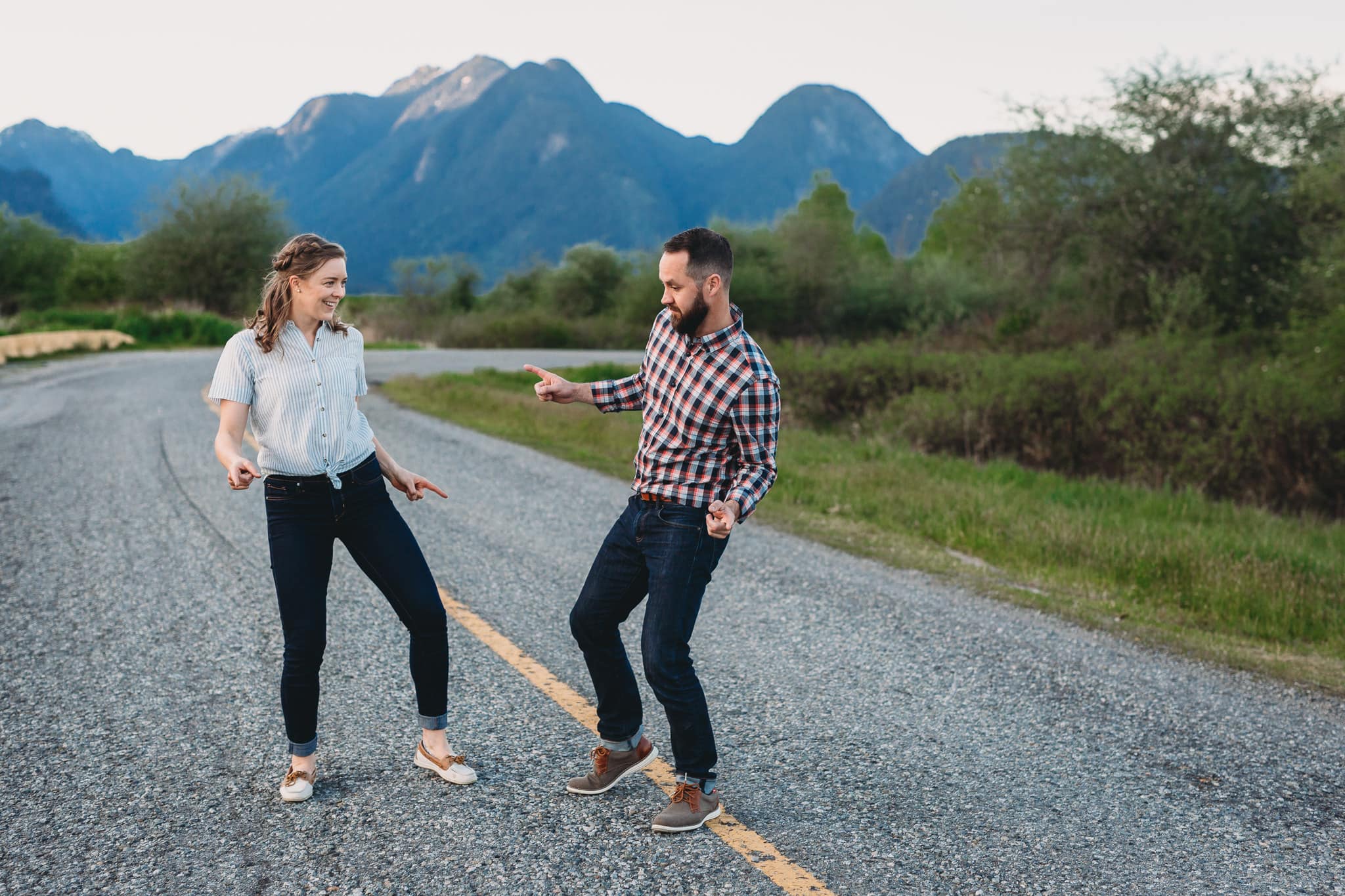fun and casual couples session at pitt lake on road with mountains in background