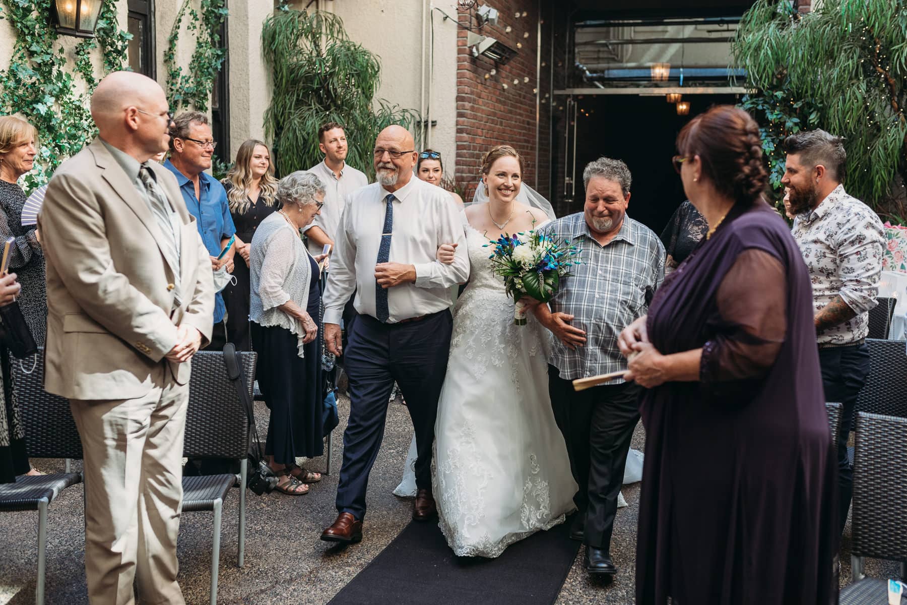 Bride with two dads walking down the aisle at Brix and Mortar Vancouver wedding ceremony